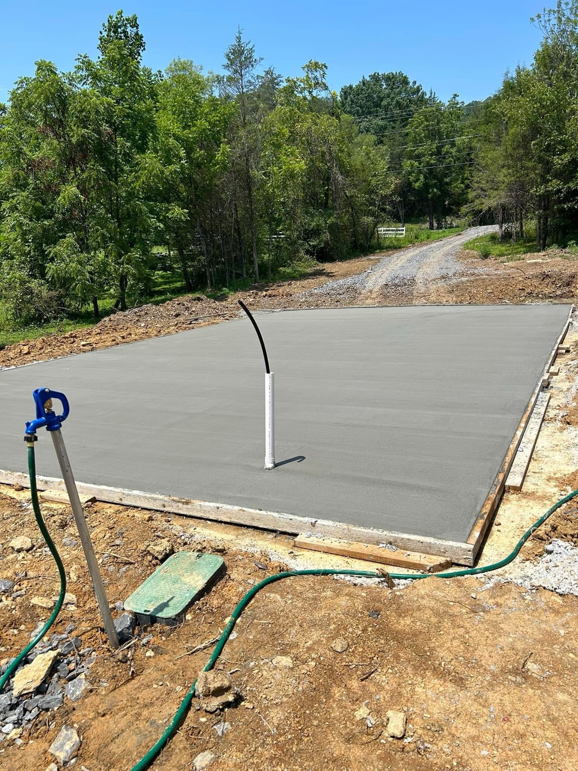 Freshly finished concrete pad beside a gravel driveway